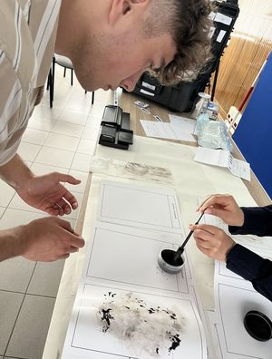 chłopak przyglądający się pracy technika nad kartką z zabezpieczonymi śladami daktyloskopijnymi