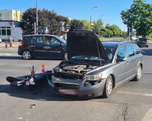 volvo z rozbitą szybą maską do góry obok leżący motorower