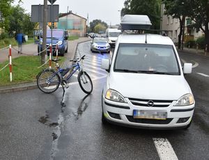 biały opel obok niego rower na ulicy za nimi radiowóz i rząd samochodów