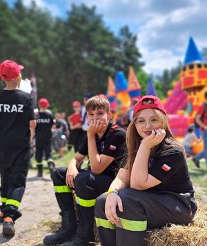 dziewczyna i chłopak w strażackich strojach siedzący na belkach słomy