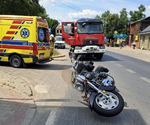 na ulicy leży czarny motocykl obok stoją wozy pogotowia i straży pożarnej