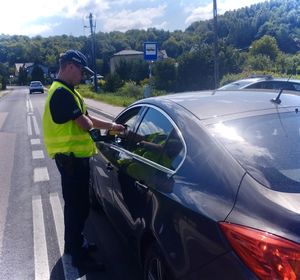 policjant przy grafitowym samochodzie na ulicy badający trzeźwość kierowcy