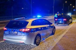 policjanci kontrolujący czarną hondę za nią radiowóz na światłach