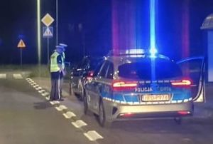 radiowóz obok policjanci kontrolujący kierowcę samochodu stojącego przed radiowozem