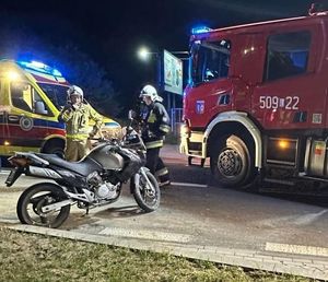 dwóch strażaków obok motocykla w tle wóz strażacki i karetka pogotowia