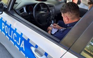 policjant siedzący w radiowozie wpisujący dane z dowodu do notatnika służbowego