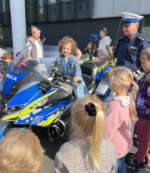 dziewczynka na motocyklu policyjnym obok inne dzieci i policjant w białej czapce