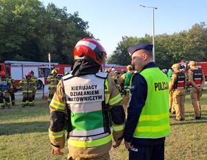 komendanci policji i straży stojący przed grupą strażaków