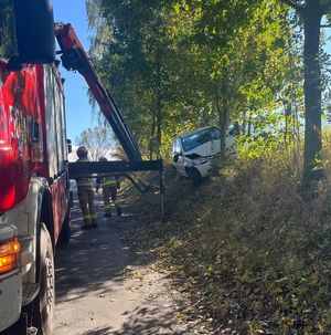 biały opel corsa z rozbitym na drzewie przodem obok strażacy