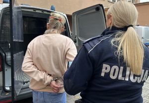 policjantka wprowadzająca kobietę w kajdankach do radiowozu z kratą