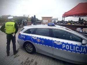 policjant obok radiowozu przed cmentarzem