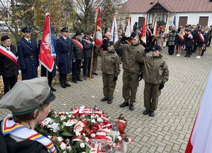 delegacja klasy mundurowej oddająca honor przed pomnikiem w tle poczty sztandarowe