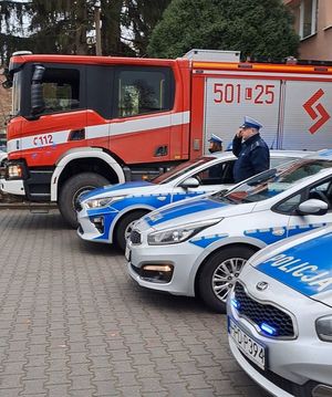 policjanci na tle wozu strażackiego oddają honor