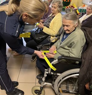 policjantka zakładająca opaskę odblaskową na wózku inwalidzkim seniorki