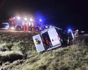 rozbity biały bus w rowie obok niego strażacy, wyżej na drodze wóz strażacki