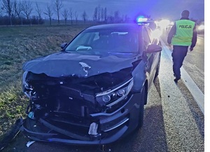 grafitowa KIA z rozbitym przodem obok policjant w kamizelce ostrzegawczej