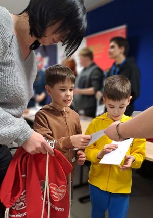 kobieta z dwoma chłopcami odbierającymi pakiety na WOŚP