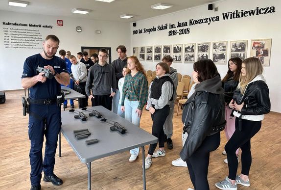 policjant prezentujący broń grupie uczniów