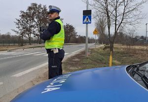 policjant z miernikiem prędkości przy radiowozie stoi przy drodze