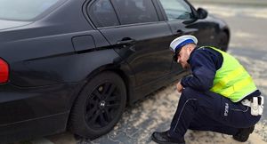 policjant oglądający koło w czarnym BMW