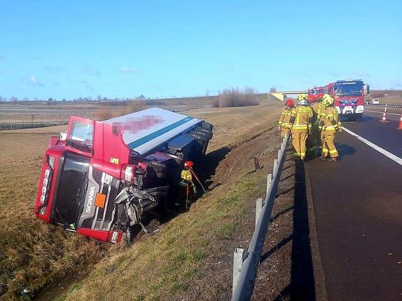 ciężarowa scania leżąca na boku w rowie, na ulicy strażacy