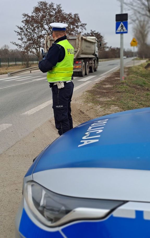 policjant przy drodze patrzący na przejeżdżającą ciężarówkę