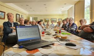 seniorzy przy stole na nim otwarty laptop z prezentacją oszustwa na wnuczka