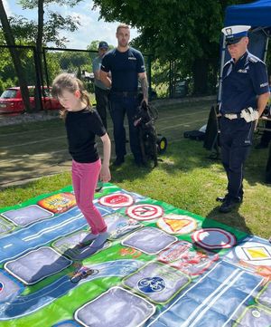policjanci patrzący na dziewczynkę skaczącą po terenowej grze planszowej