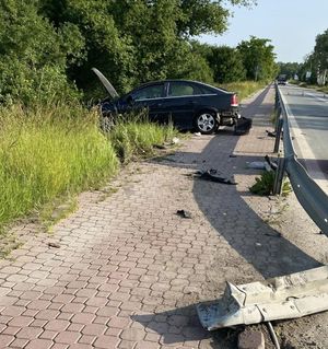 czarny opel stojący częściowo na chodniku za barierą częściowo w krzakach