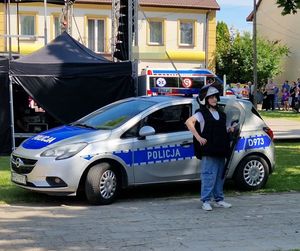 chłopiec z policyjna tarczą w kamizelce pozujący obok radiowozu