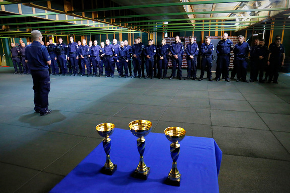 Funkcjonariusze ubrani w mundur koloru granatowego z napisami policja biorący udział w turnieju. Zdjęcie wykonane na strzelnicy policyjnej, gdzie policjanci zapoznają się z regulaminem turnieju