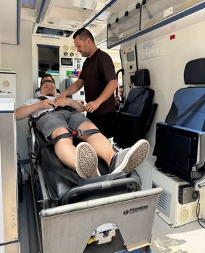 dwóch mężczyzn w karetce, jeden leży na łóżku przypięty pasami drugi nad nim stoi