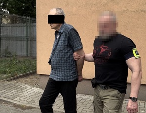 policjant prowadzący zatrzymanego mężczyznę w kajdankach