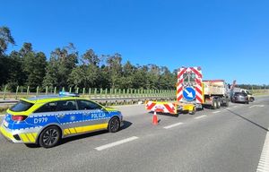 radiowóz na miejscu kolizji na drodze s12 przed nim samochód służby drogowej z przyczepką i znakami drogowymi obok niego ford który uderzył w przyczepkę
