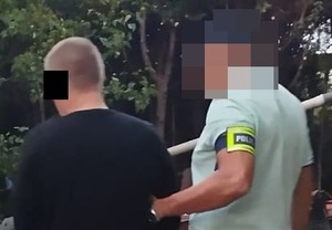 policjant prowadzący mężczyznę w kajdankach