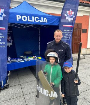 policjant dzielnicowy z dziećmi trzymającymi tarczę