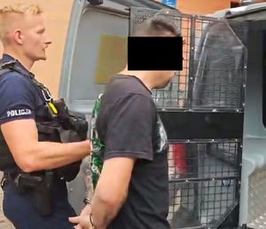 policjant prowadzący zatrzymanego w kajdankach