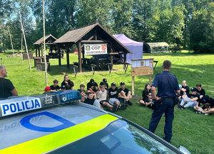 policjant stojący przed dziećmi siedzącymi na trawie