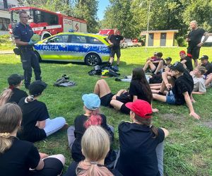 policjant trzymający arbuza przed grupą obozowiczów