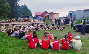 policjanci podczas spotkania z dziećmi siedzącymi na trawie w kręgu