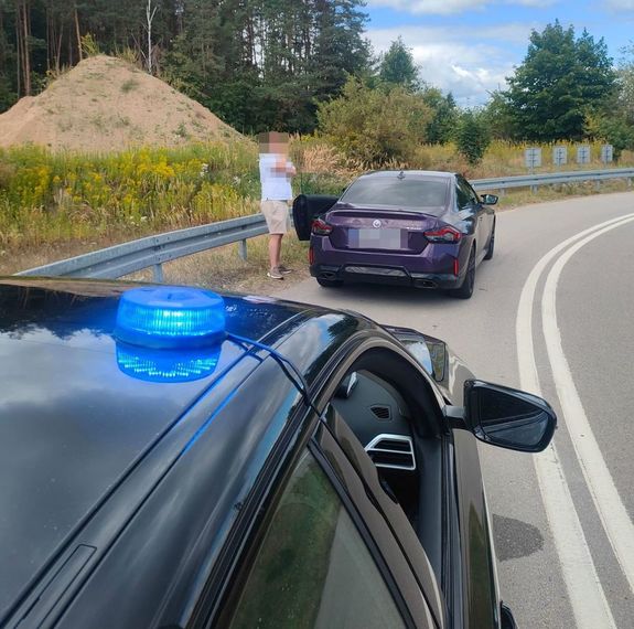 zanonimizowany mężczyzna stojący obok BMW na tle policyjnej lampy na dachu radiowozu