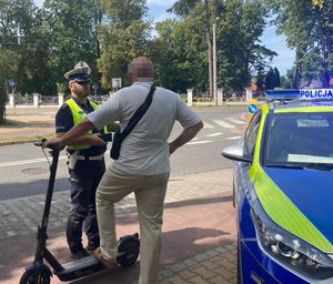 policjant legitymujący mężczyznę z hulajnogą obok stoi radiowóz