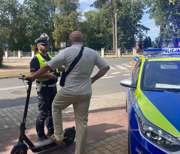 policjant legitymujący mężczyznę z hulajnogą obok stoi radiowóz