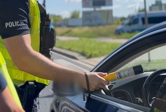 policjant przy samochodzie trzymający urządzenie do badania na trzeźwość