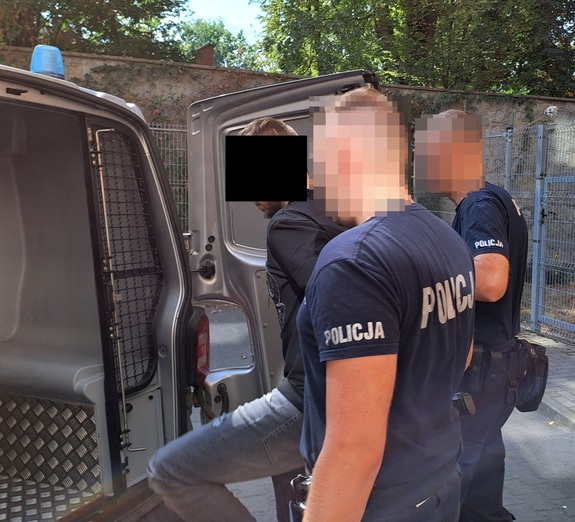 policjanci wprowadzający zatrzymanego do policyjnego busa