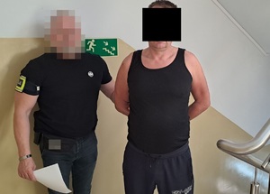 policjant trzymający zatrzymanego mężczyznę za ramię. Zatrzymany w kajdankach