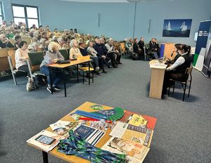 sala wykładowa ze słuchaczami na pierwszym planie stolik z gadżetami reklamowymi ZUS