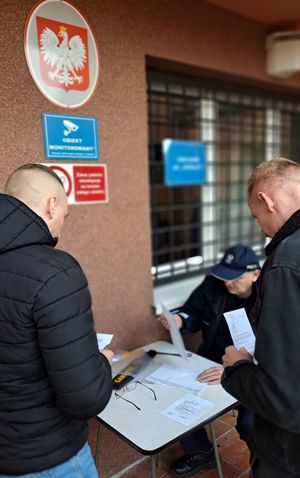 punkt kontrolny przed budynkiem i dwóch mężczyzn zgłaszających się u mężczyzny siedzącego przy stoliku