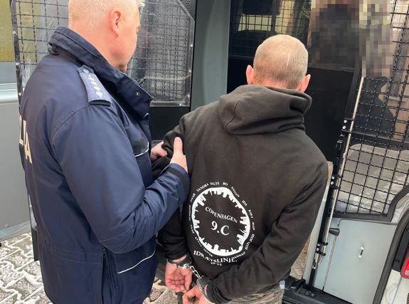 policjant wprowadzający mężczyznę w kajdankach do okratowanego radiowozu