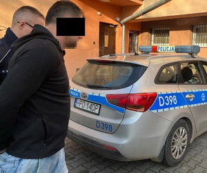 policjant prowadzi mężczyznę w kajdankach do radiowozu